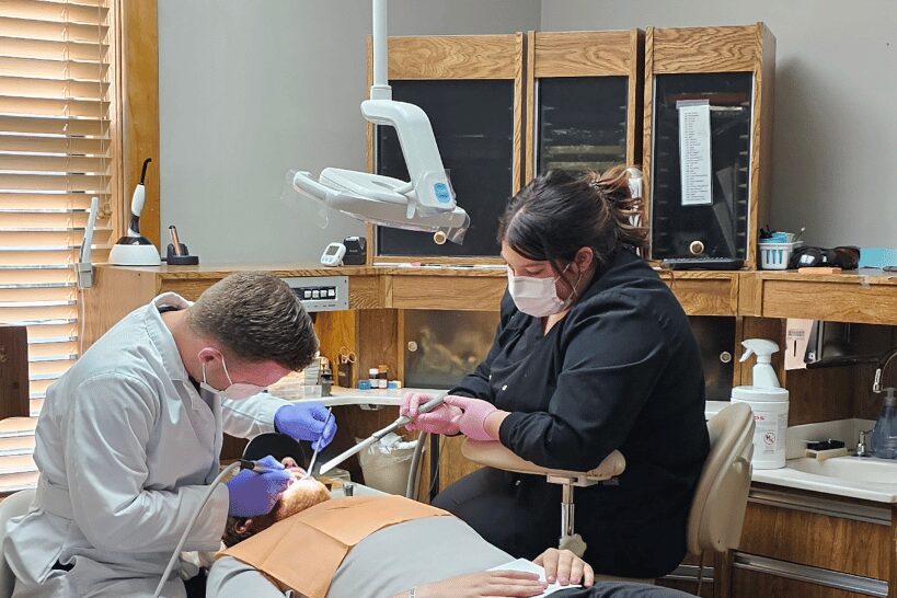 Dr. Anthony Pulver with dental assistant performing oral surgery on patient lying in chair